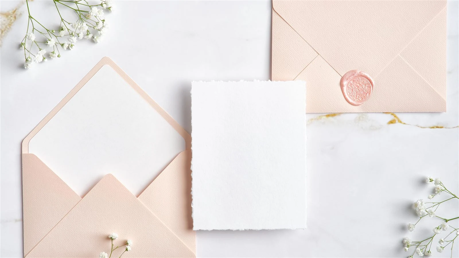 A blank card and a sealed envelope with a dark red wax rose seal, framed by fern leaves on a marble surface.